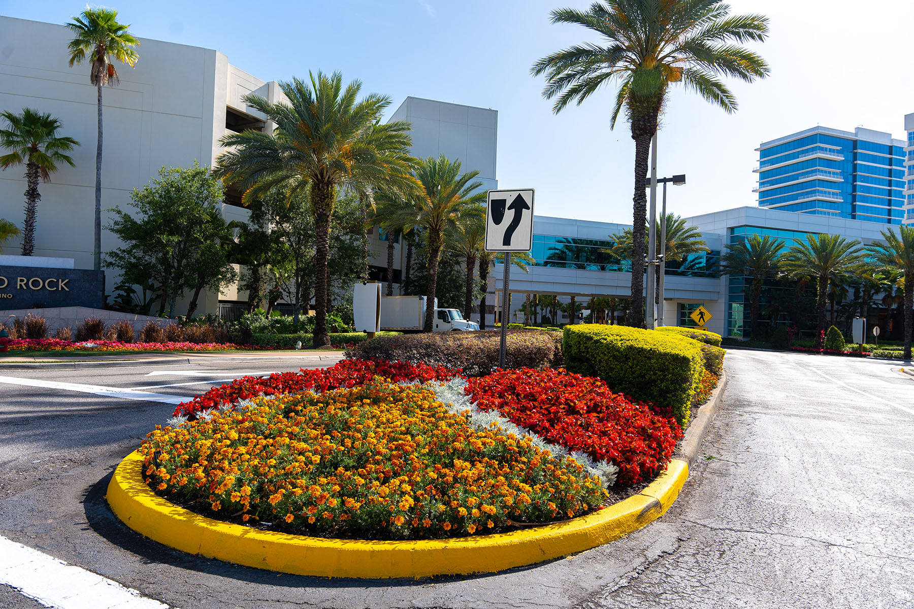 Commercial property entrance with manicured flower beds, palms, and trimmed hedges